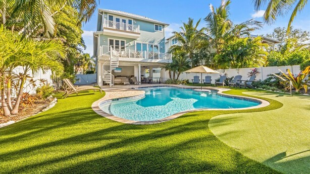 A two-story house with a swimming pool, surrounded by well-maintained lawn and palm trees.