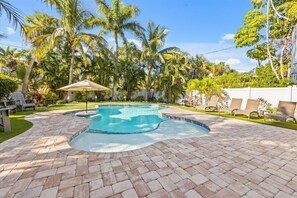 A swimming pool with a curved edge, surrounded by a brick patio, palm trees, and lounge chairs. - Big Family Beach House: Large family home, heated pool, putting green (Anna Maria)