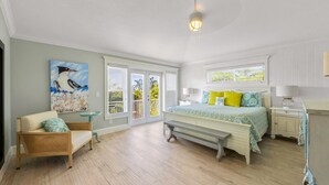 A bedroom with a bed, a chair, a bench, a painting, and a window with blinds.