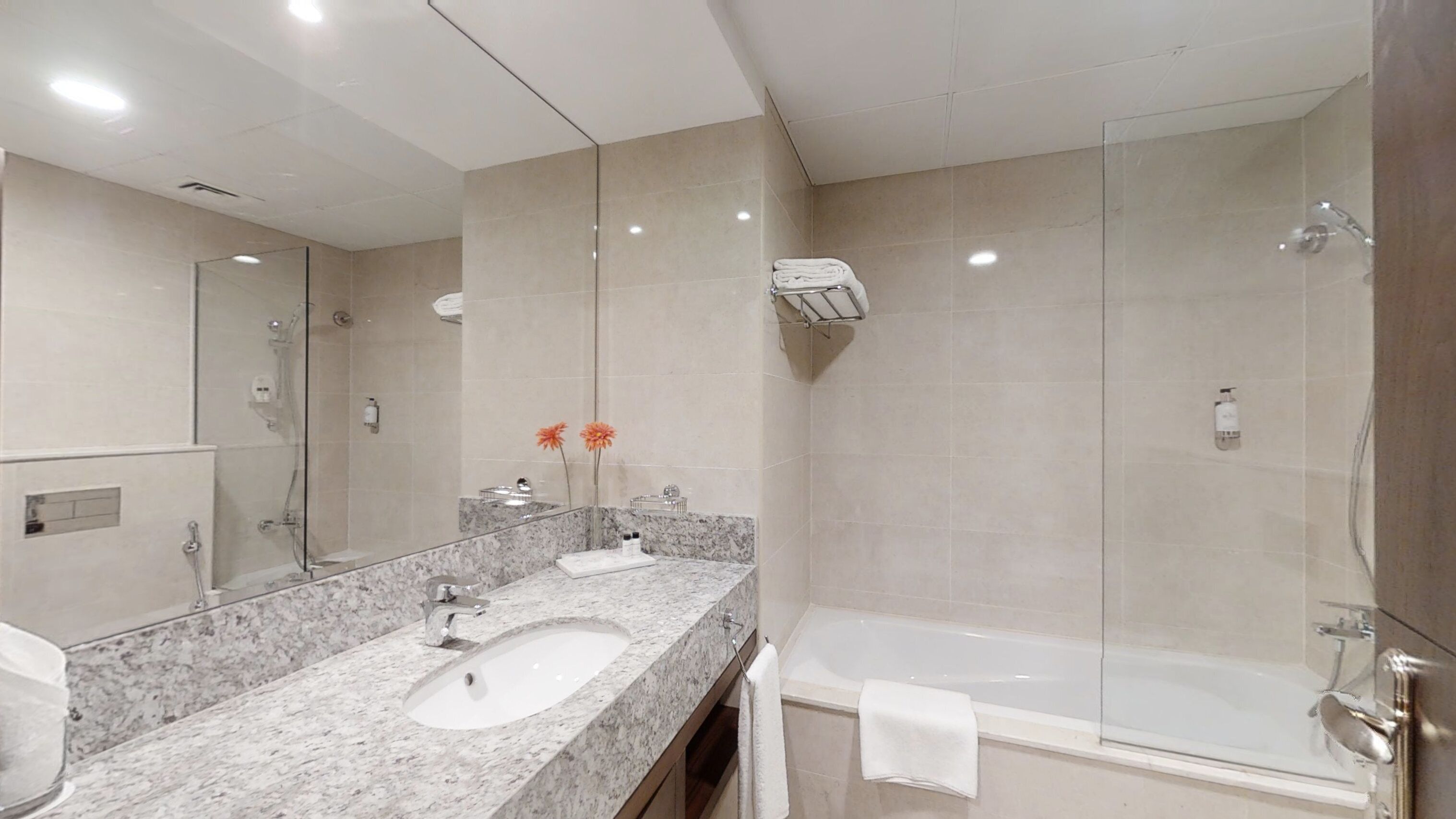 Un baño moderno con lavamanos de mármol, un espejo grande, ducha con mampara de vidrio y una bañera.