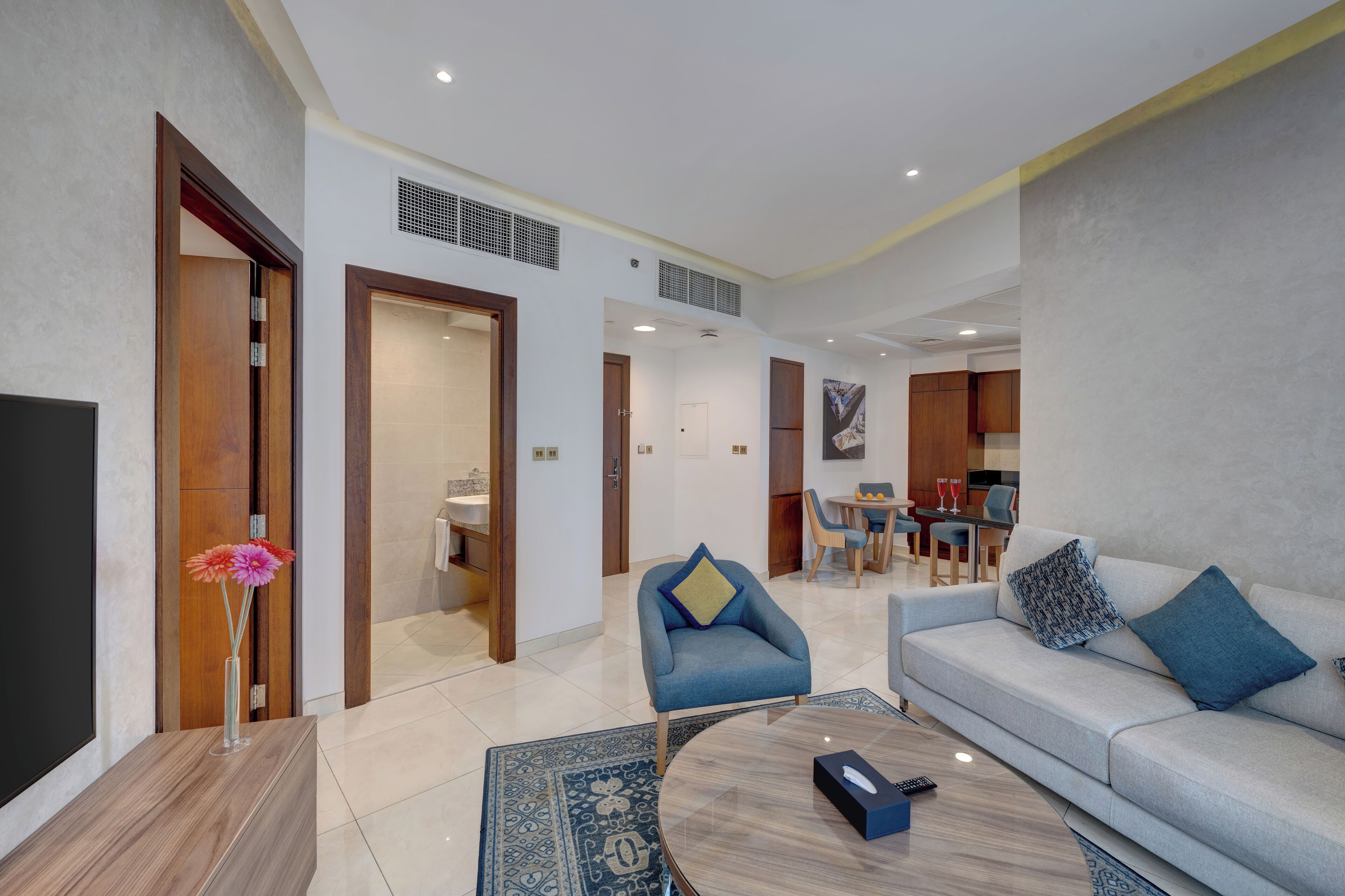 Una sala moderna con sofá, sillón y mesa de centro. Hay un televisor en un mueble bajo y un jarrón con flores.