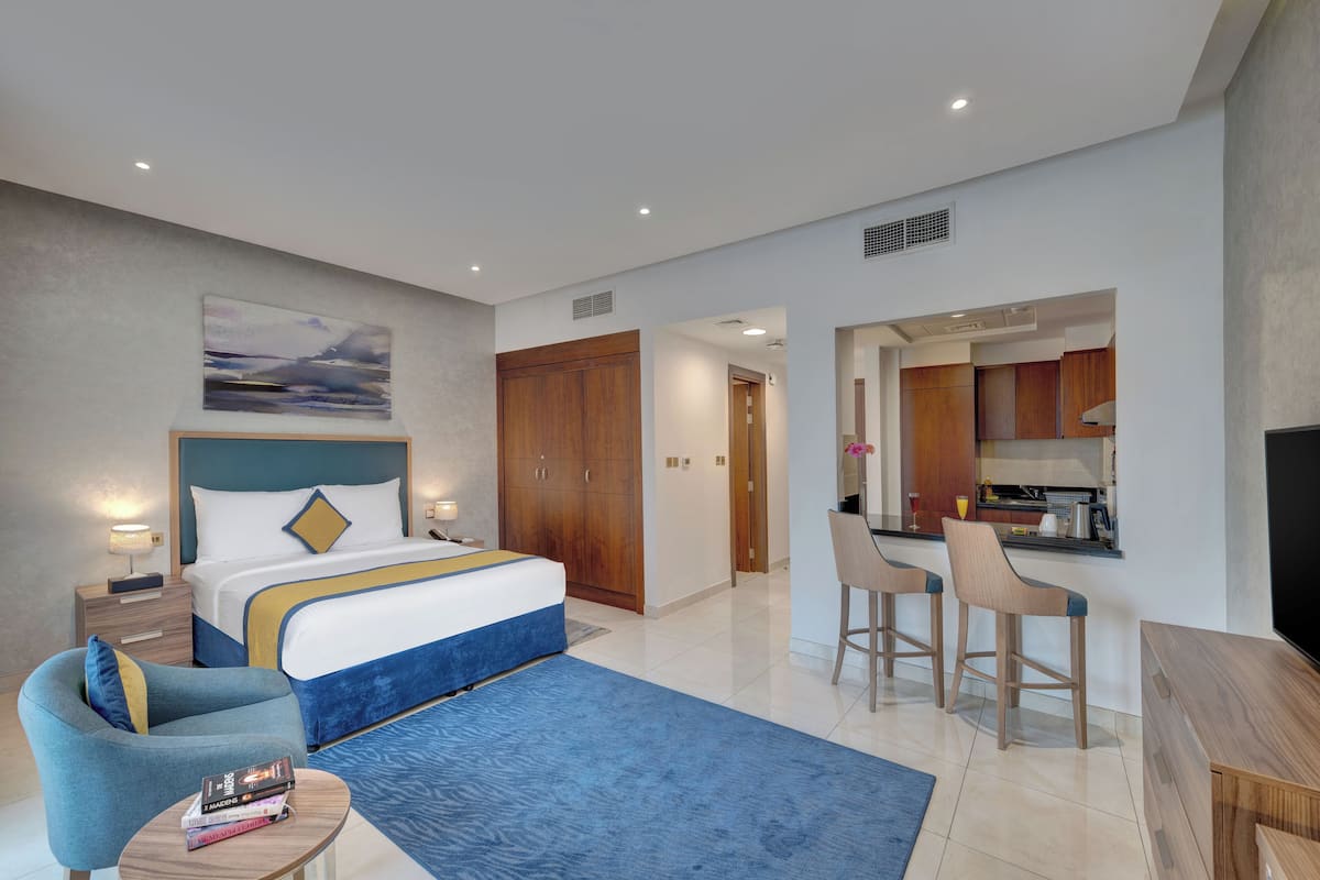 Habitación de hotel moderna con una cama grande, un escritorio, dos taburetes altos y un televisor.