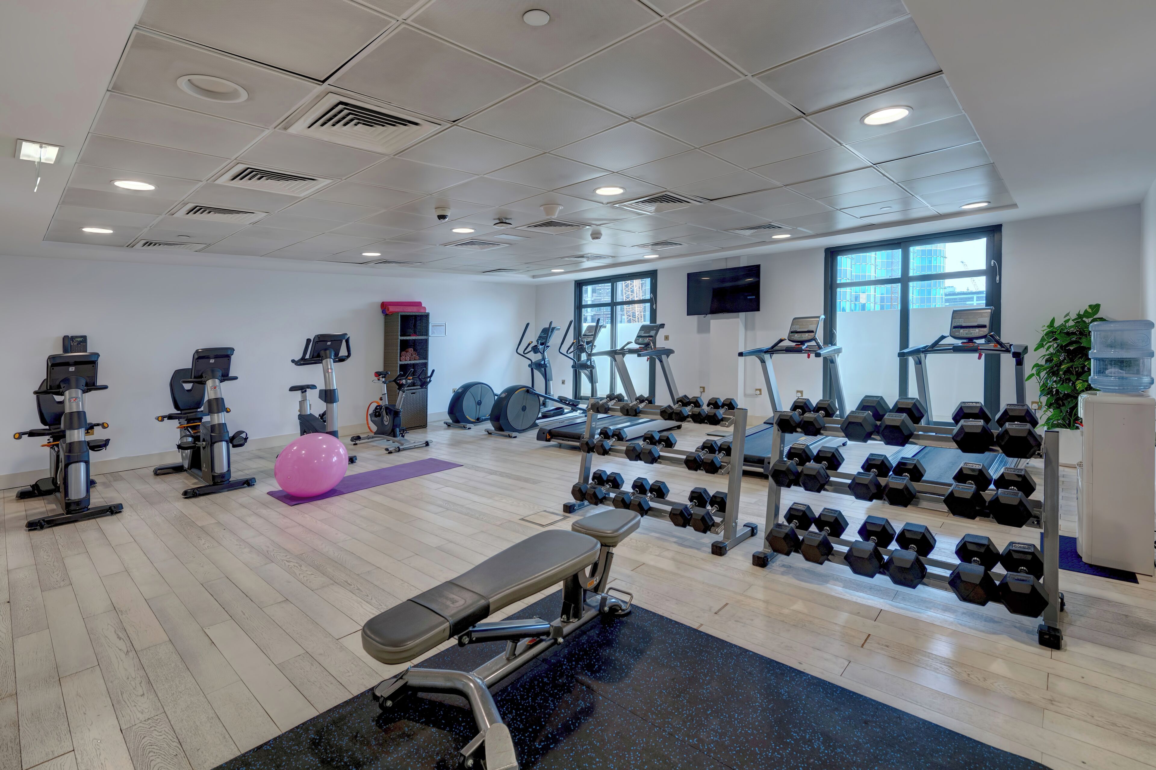 Una palestra con diverse attrezzature per l'allenamento, tra cui tapis roulant, ellittiche e pesi.