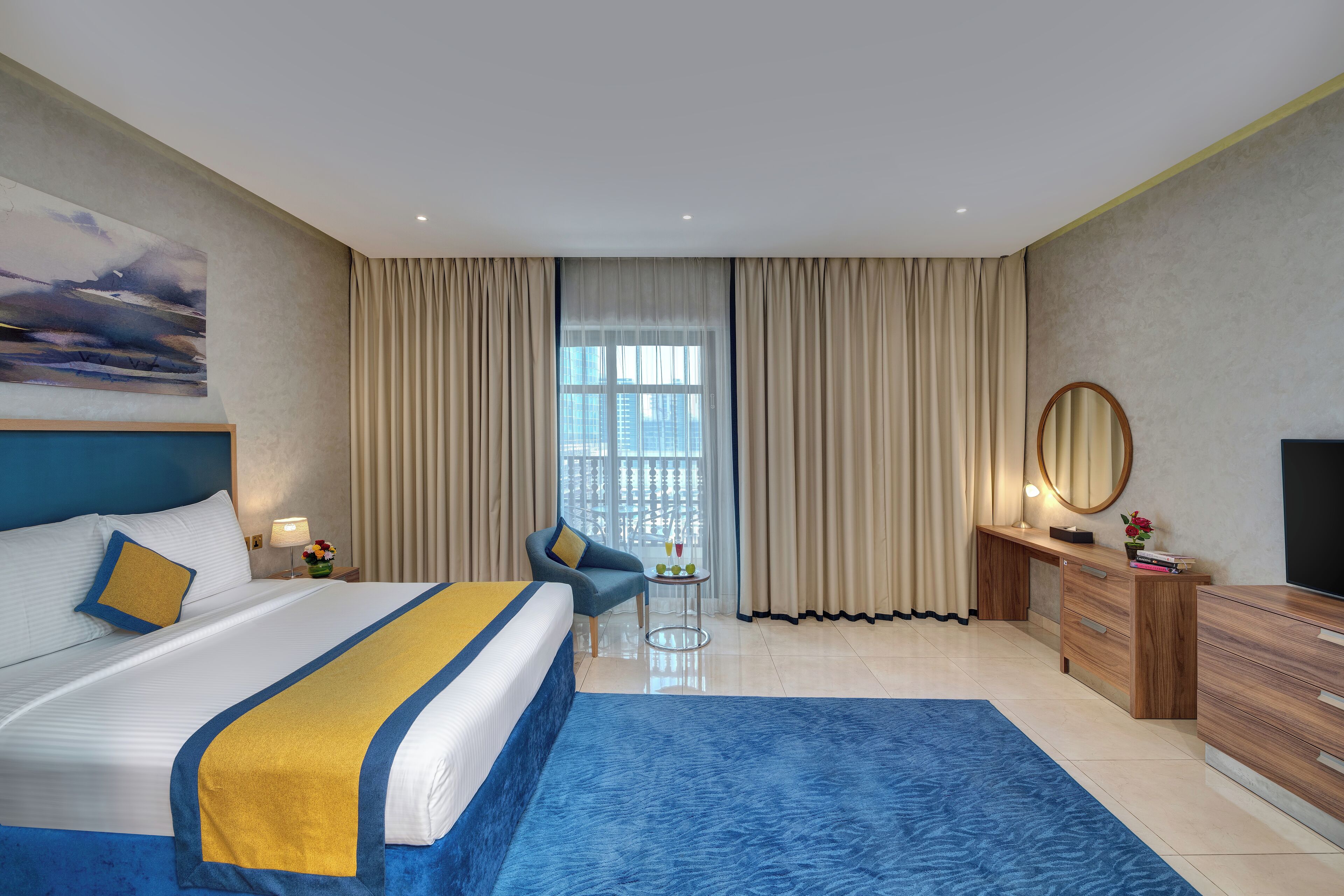 A hotel room with a large bed, a desk, a chair, a TV, and a view of the city through the window.