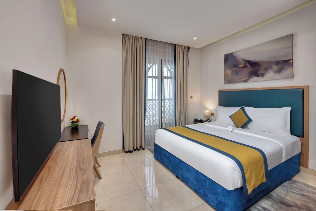 Una habitación de hotel con una cama, un escritorio, un televisor y una ventana con cortinas.