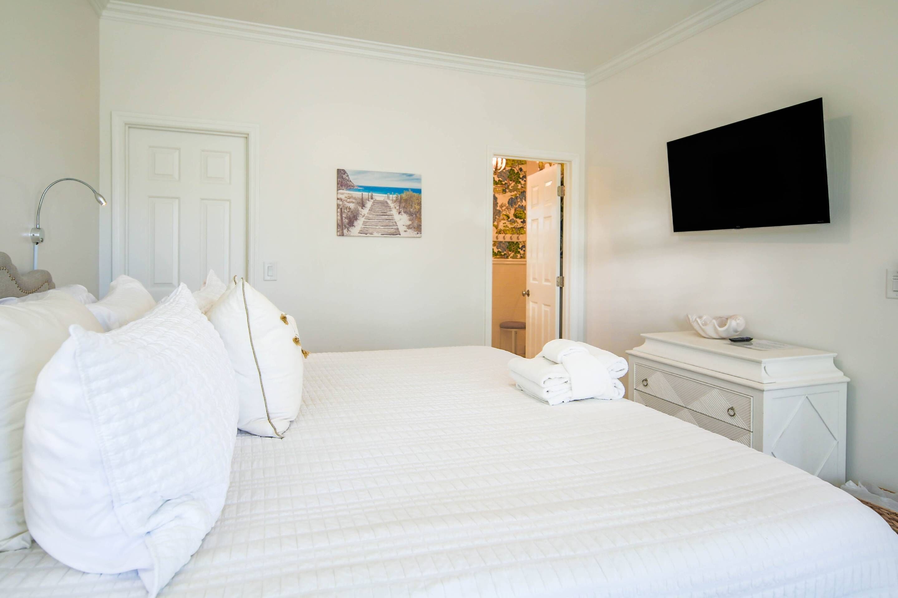 Habitación de hotel con una cama grande, un televisor de pantalla plana, un aparador blanco y una puerta que da a un baño.