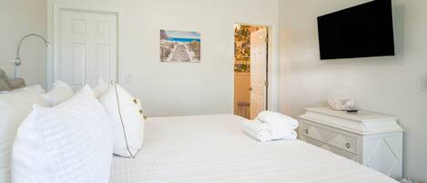 Habitación de hotel con una cama grande, un televisor de pantalla plana, un aparador blanco y una puerta que da a un baño.