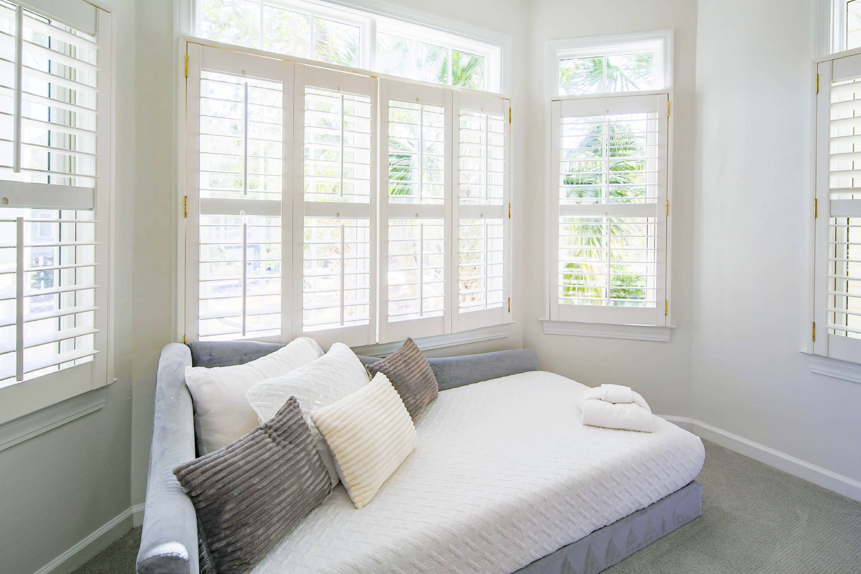 A bedroom with a large bed, multiple windows, and a view of greenery outside.