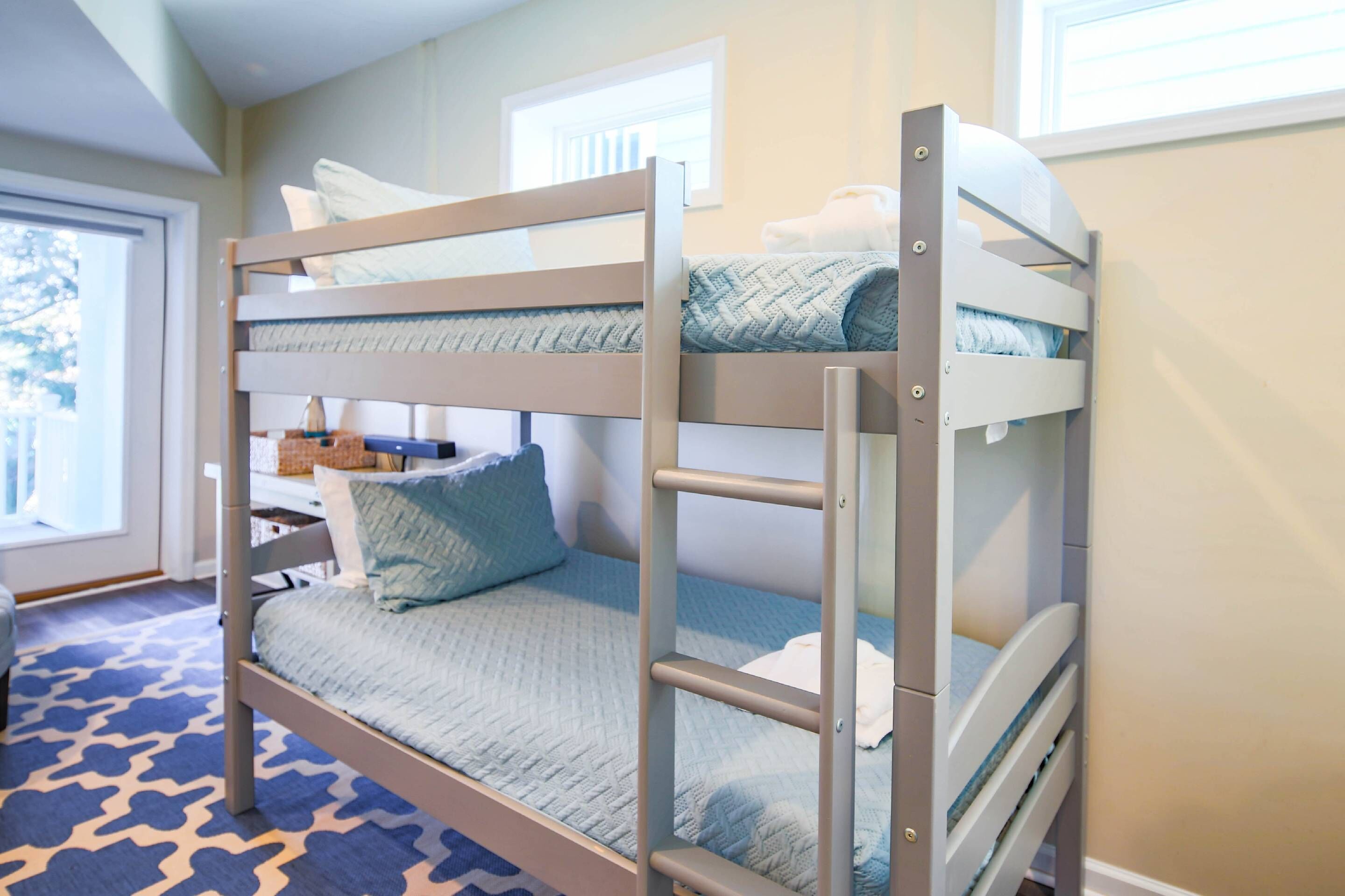 Ein Stockbett mit blauer Steppmatratze, einem weißen Kopfkissen und einem Holzrahmen.