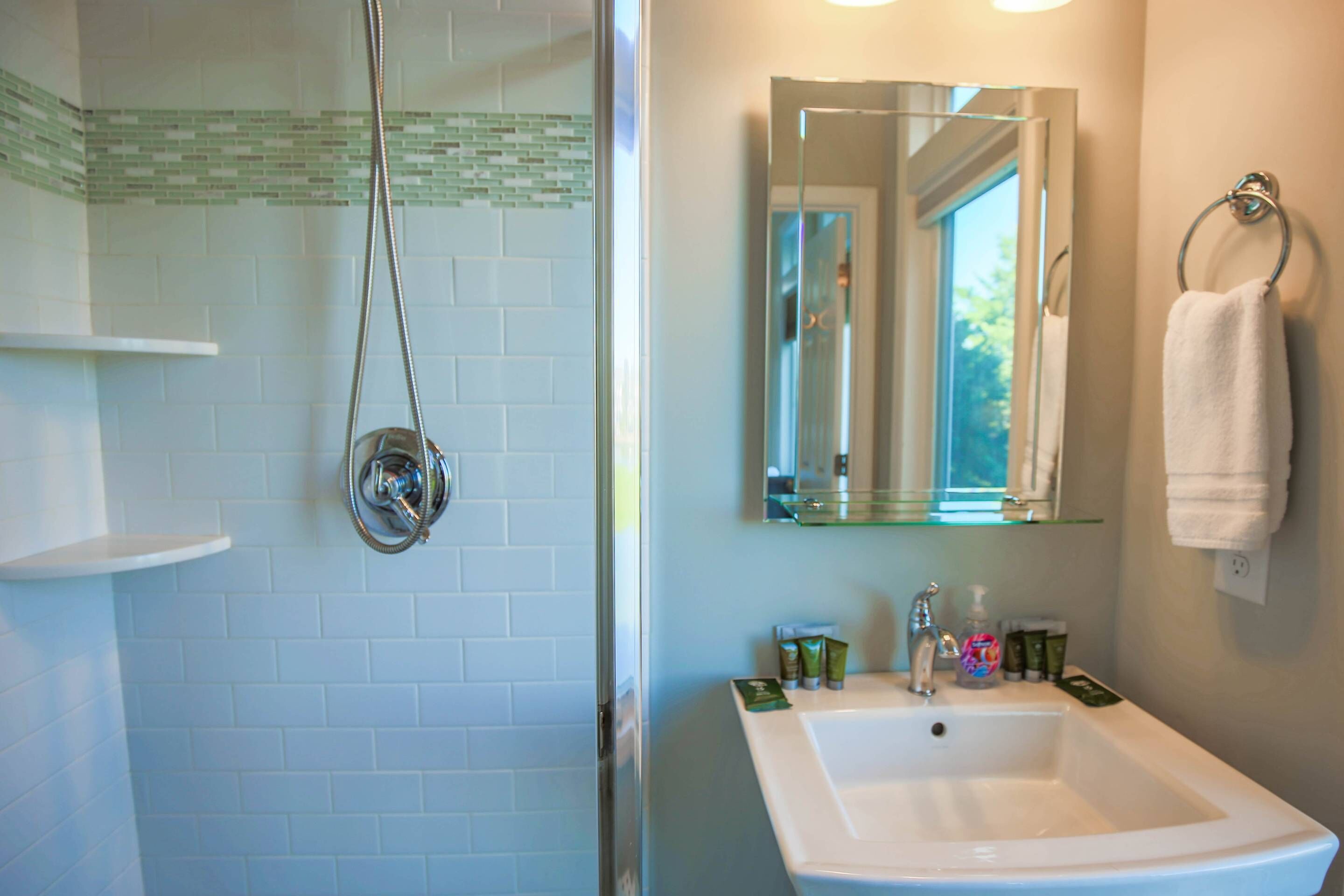 A bathroom with a glass shower enclosure, a sink with toiletries, and a mirror above the sink.