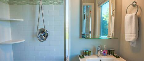 A bathroom with a glass shower enclosure, a sink with toiletries, and a mirror above the sink.