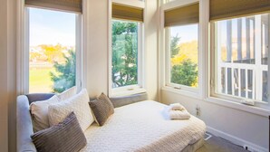Ein Schlafzimmer mit einem großen Bett, mehreren Fenstern und Blick auf eine Terrasse und Bäume.
