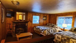 Een gezellig kamer in chaletstijl met een open haard, twee bedden met passend beddengoed, een televisie en een raam met jaloezieën.