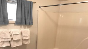 Een badkamer met een douche, toilet en wastafel. Handdoeken hangen aan de muur.