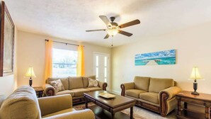 A living room with two sofas, a coffee table, a ceiling fan, and a painting on the wall. - Near Siesta Key - single story pet friendly (Sarasota)
