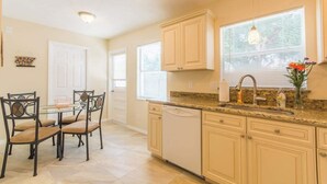 A kitchen with a glass-top dining table, chairs, a dishwasher, cabinets, and a window with blinds. - Near Siesta Key - single story pet friendly (Sarasota)