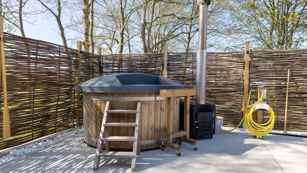 Un bain à remous avec une structure extérieure en bois, une échelle et un tuyau.