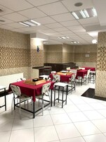 Un comedor con mesas y sillas, una zona de cocina y piso de baldosas.