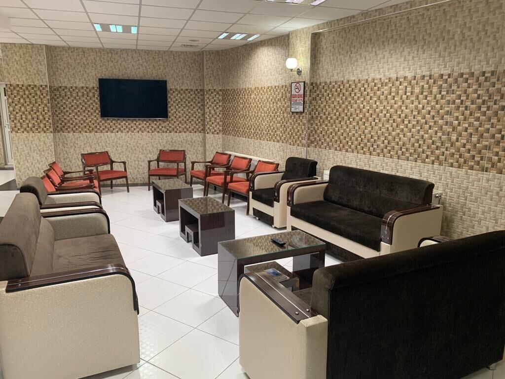 Eine Lounge mit verschiedenen Sitzgelegenheiten, darunter Sofas und Sessel, einem Wand-Fernseher und einer Wandgestaltung mit Fliesen.