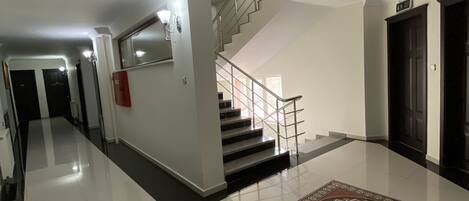 Un pasillo amplio con piso pulido, una escalera con barandilla de metal y una alfombra decorativa.