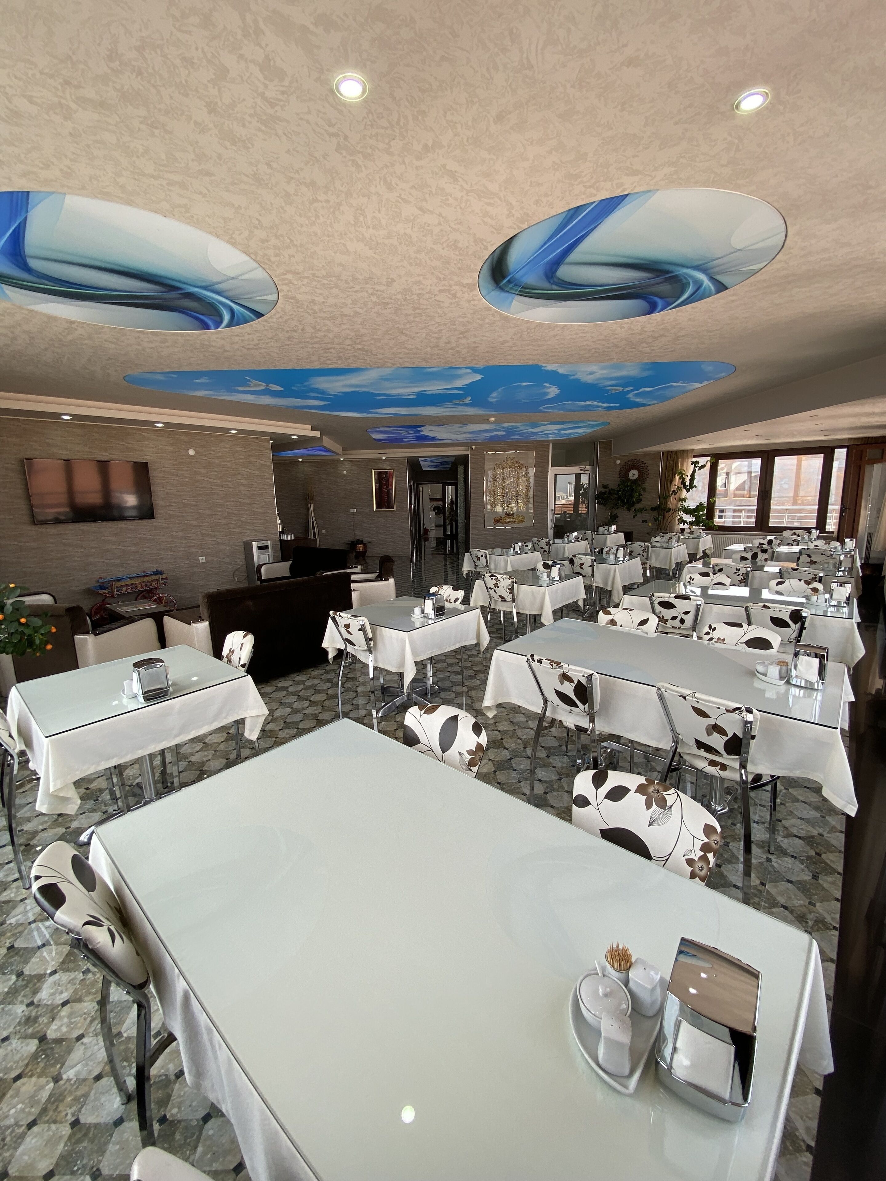 Un comedor amplio con varias mesas y sillas, un televisor de pantalla plana montado en la pared y un techo con diseño de nubes.