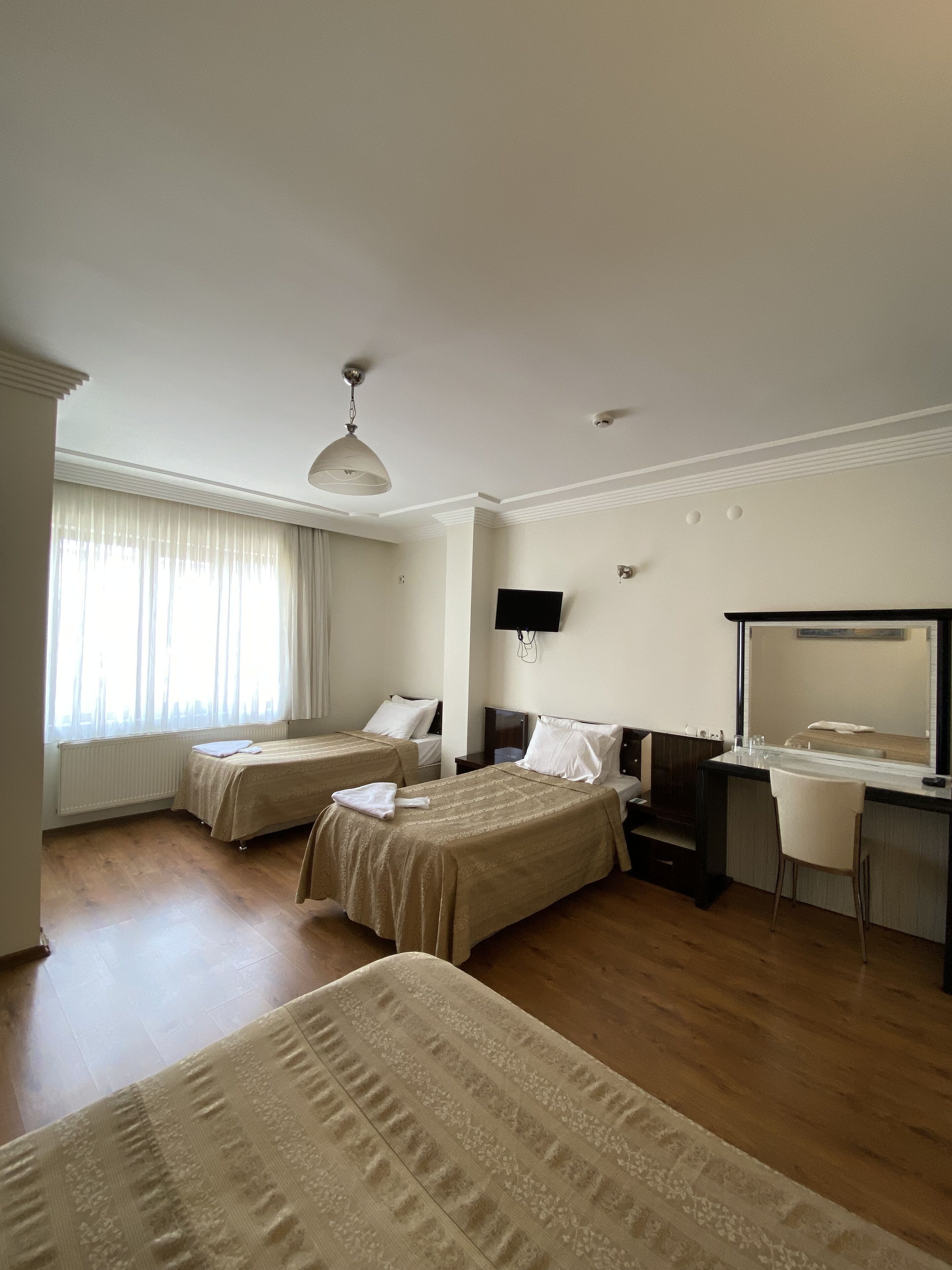 Habitación de hotel con dos camas, un escritorio, una silla, un espejo grande y una ventana con cortinas.
