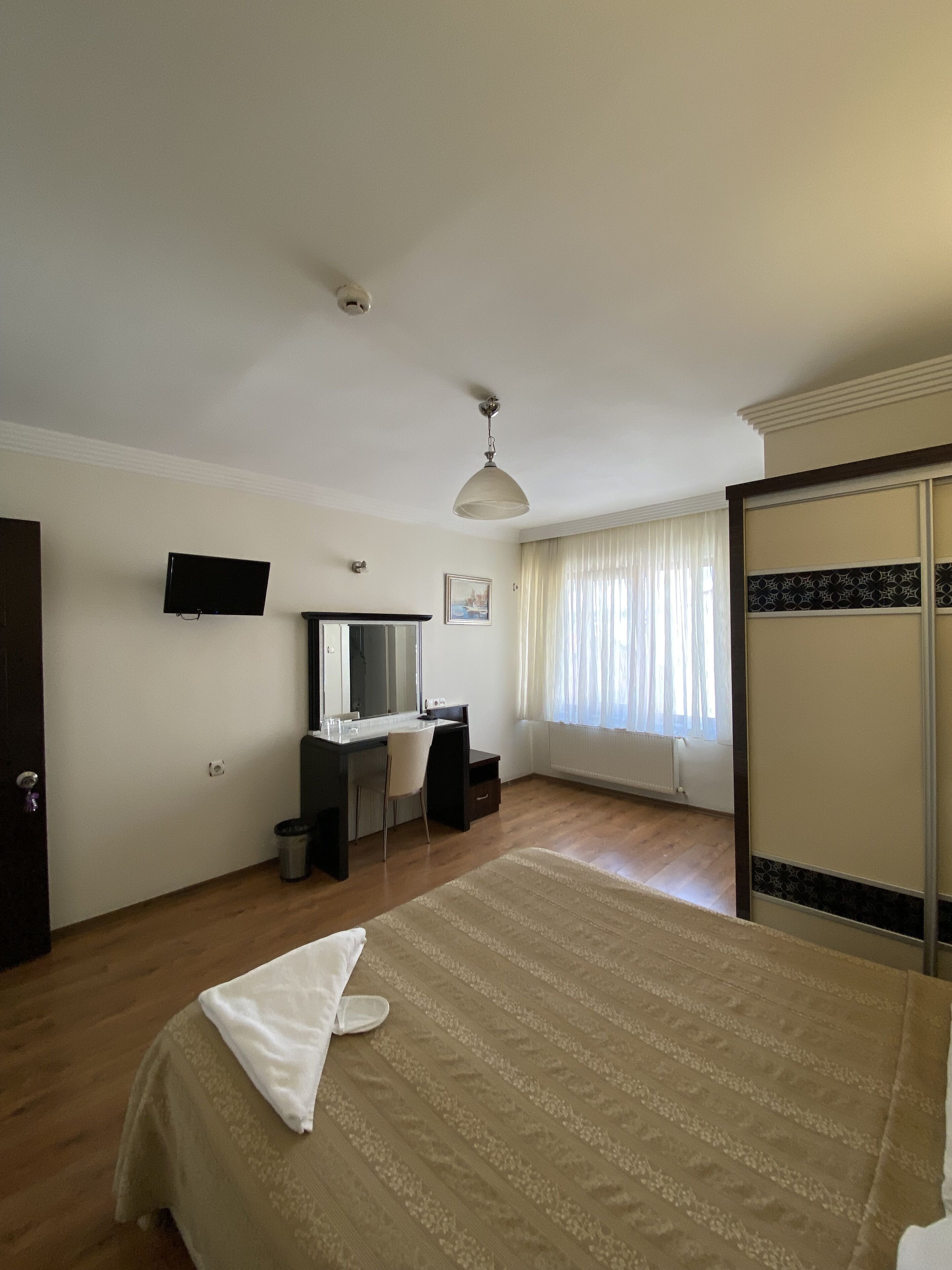 A hotel room with a bed, a desk with a chair, a television, and a wardrobe.