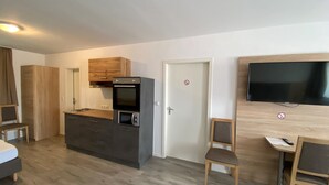 Een kleine keuken met een ingebouwde oven en magnetron, een houten kastje boven het aanrecht, een aan de muur bevestigde televisie, en een deur met een rookvrij bordje.