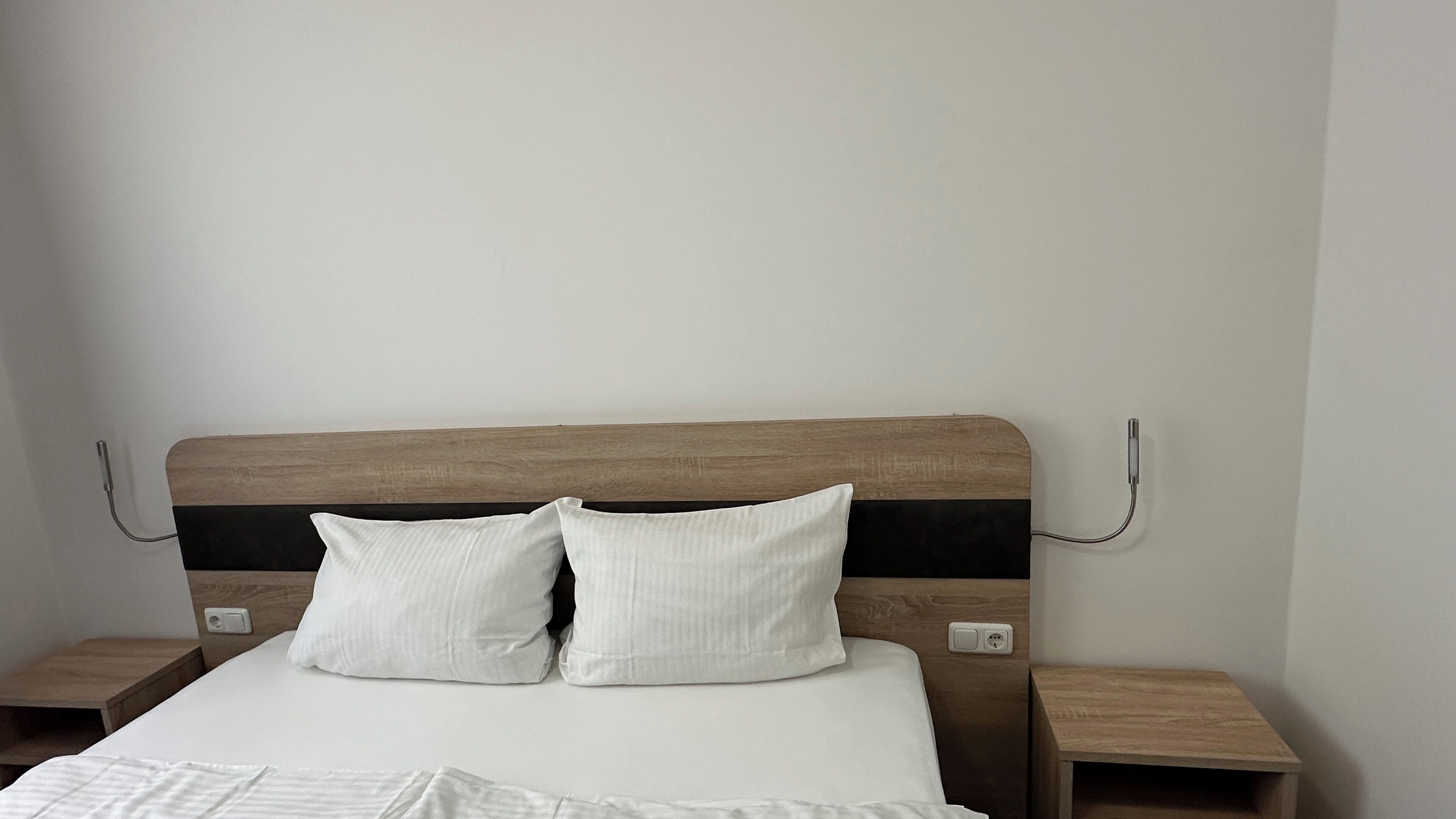 Un lit avec une tête de lit en bois, deux oreillers blancs et un couvre-lit blanc. Il y a deux tables de chevet avec un placage en bois.