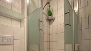 Een moderne badkamer met een douche met glazen wand, een toilet en een kleine potplant aan de muur.