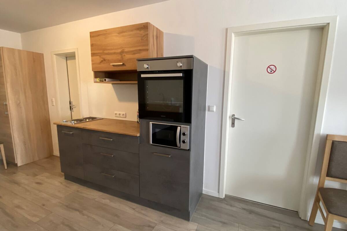 A compact kitchen with a built-in oven, microwave, and a wooden cabinet above the countertop.