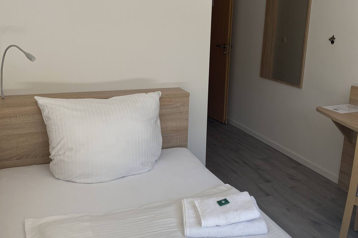 A hotel room with a bed, a wooden headboard, a bedside table, a mirror, and a door leading to another room.