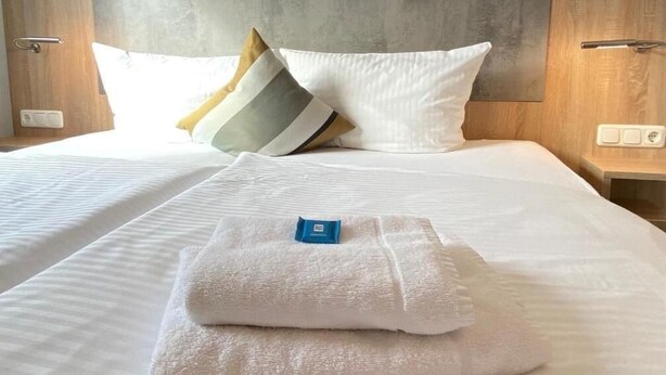 Een hotelkamer met een net opgemaakt bed, een hoofdbord met een structuur en een nachtkastje met een stopcontact.
