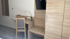 Een moderne kamer met een houten bureau, een stoel, een aan de muur bevestigde televisie en een kledingkast.