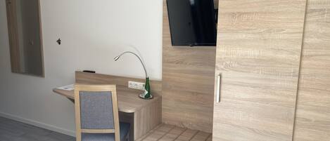 Una habitación moderna con un escritorio de madera, una silla, un televisor en la pared y un armario.