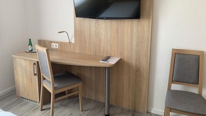 Een moderne kamer met een houten bureau, een stoel, een aan de muur bevestigde televisie en een klein kastje.