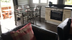 Une cuisine avec une table à manger pour quatre personnes, un canapé en cuir noir et une fenêtre donnant sur un jardin.