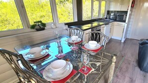 Un coin repas avec une table en verre pour quatre personnes, une cuisine équipée d’appareils modernes et une vue sur la verdure environnante.
