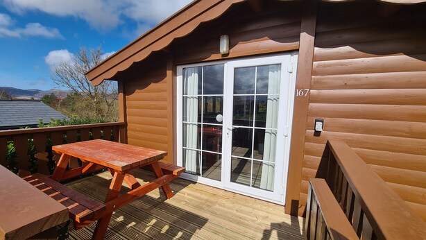 Une cabane en bois dotée d’une porte coulissante en verre, d’une table de pique-nique et d’une terrasse.