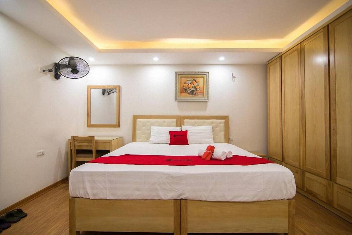 A hotel room with a bed, a bedside table, a mirror, a fan, and a wardrobe.