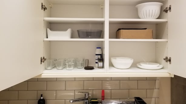 Una cocina con armarios blancos, salpicadero de azulejos y diversos utensilios, como vasos, cuencos y una botella.