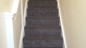 Una escalera con peldaños alfombrados en tono oscuro y barandillas blancas.