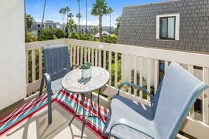 Ein Balkon mit Tisch und zwei Stühlen, einer karierten Teppich und Blick auf eine Wohngegend mit Palmen und Häusern.