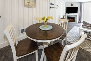 Een eetruimte met een ronde tafel, witte stoelen, een vaas met gele bloemen, een ingelijste foto aan de muur en een open haard met een televisie erboven.