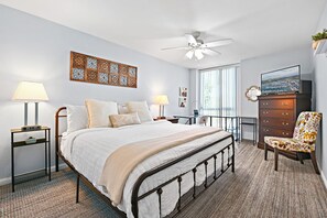 Une chambre à coucher comprenant un lit, des tables de chevet, un bureau, une chaise, une commode, un ventilateur de plafond et des œuvres d’art accrochées aux murs.