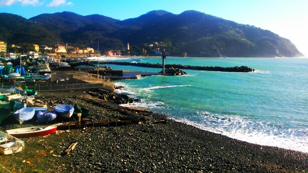 Una zona costera amb embarcacions amarrades a la riba, una platja rocosa i una muntanya de fons.