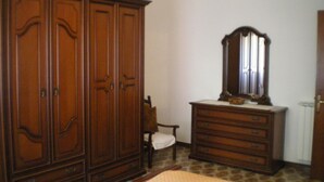 Ein Schlafzimmer mit großem Holzschrank, einer Kommode mit Schubladen, einem Sessel und einem Spiegel.