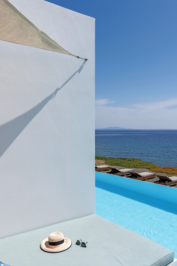 A poolside area with a view of the sea, a lounge chair, a hat, and sunglasses.
