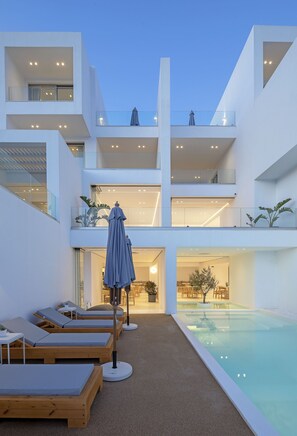 A modern building with multiple balconies, a swimming pool, and sun loungers.