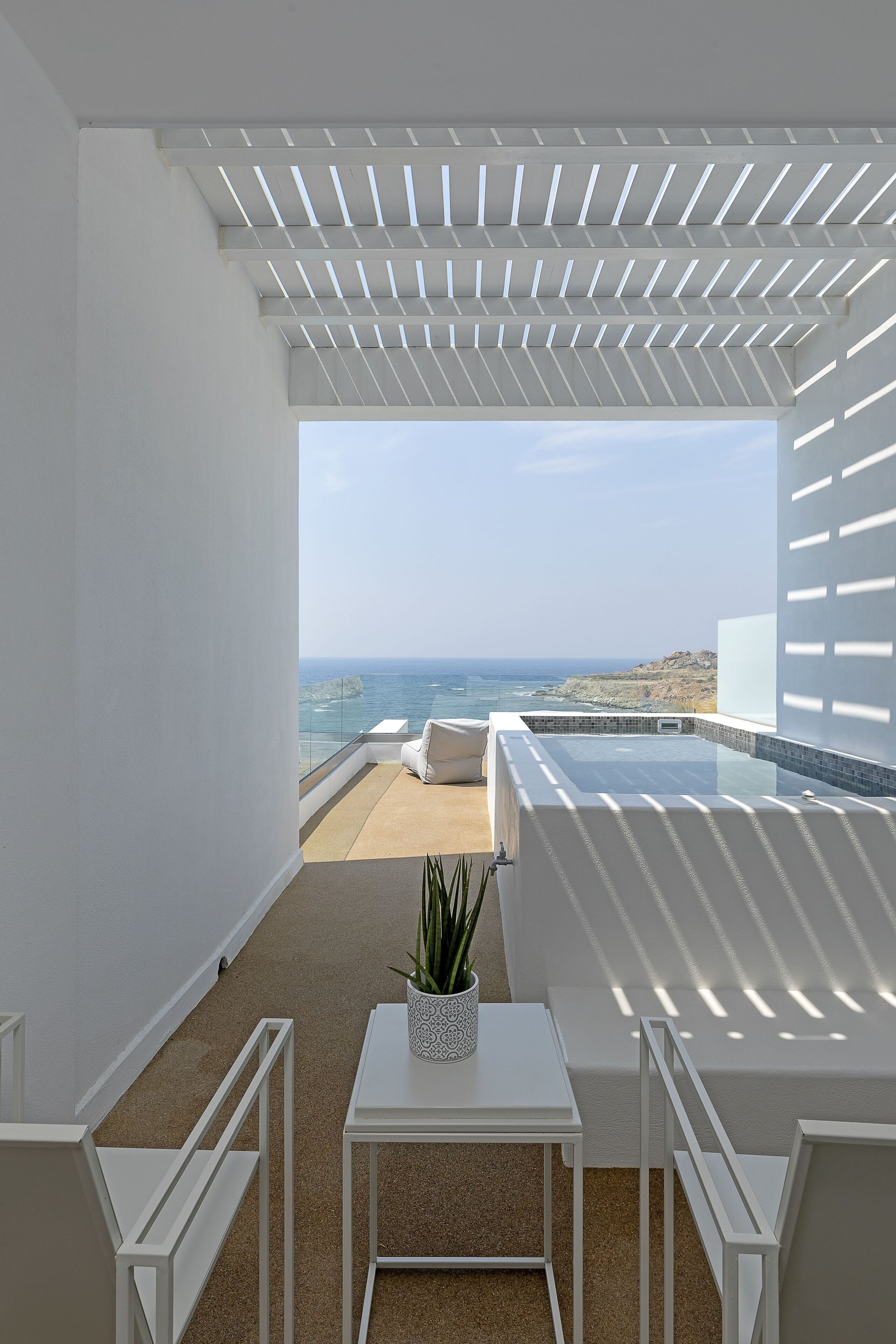 Un balcon avec vue sur l’océan, une petite piscine et des meubles blancs.